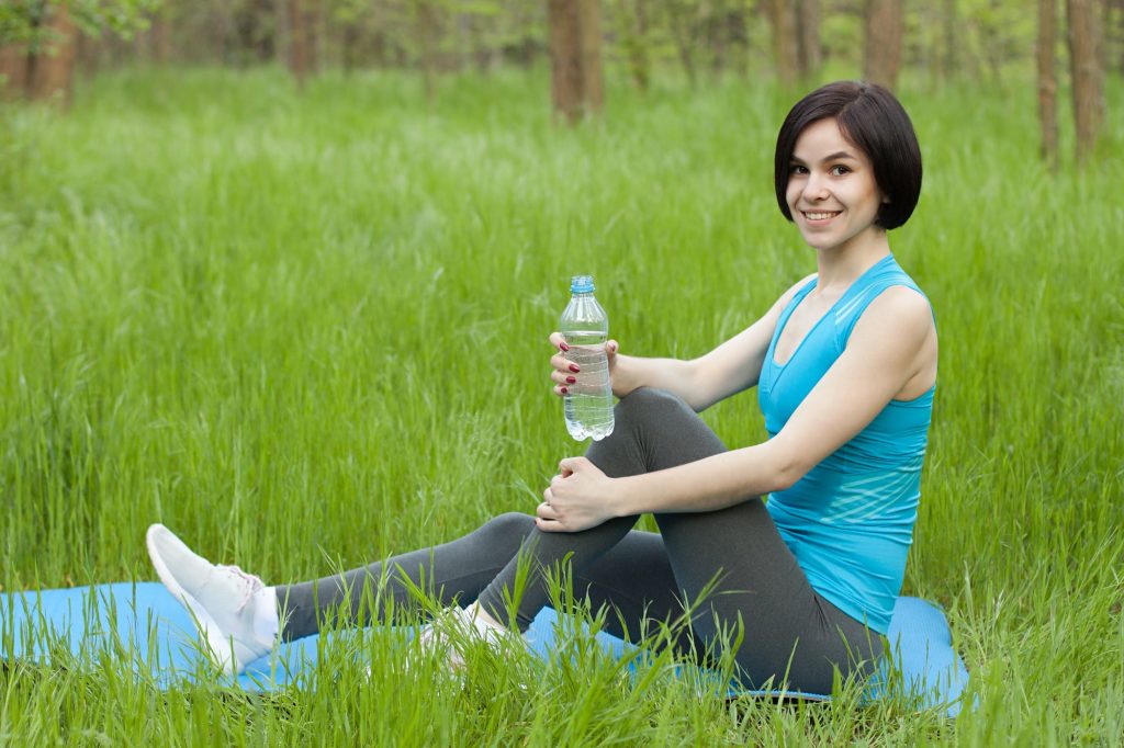 woman in blue tank top and black pants sitting on green grass field